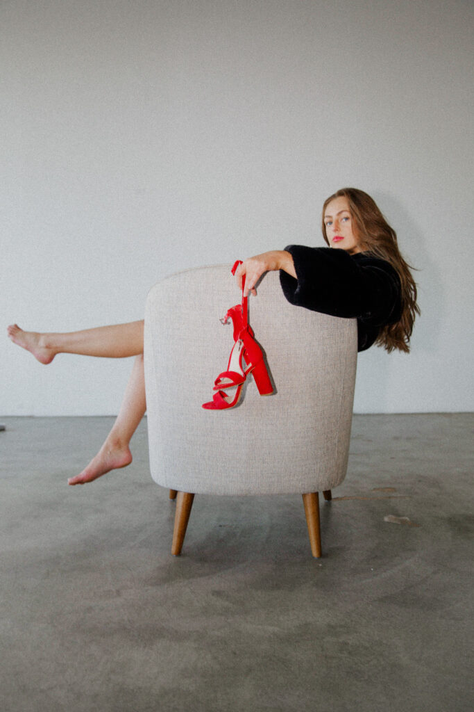 Girl in chair holding red high heel shoes