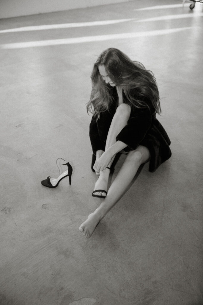 Young female model sits on floor and puts on high heels